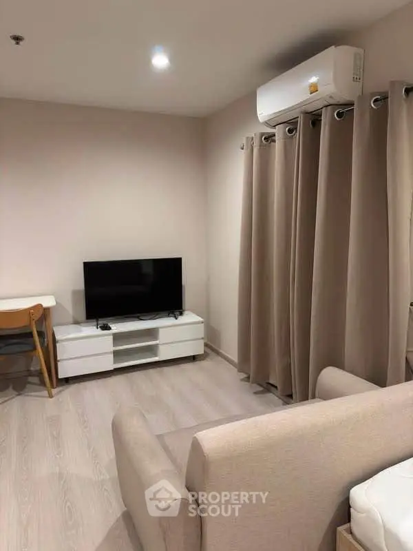 Modern living room with sleek furniture and neutral tones, featuring a wall-mounted TV and air conditioning.