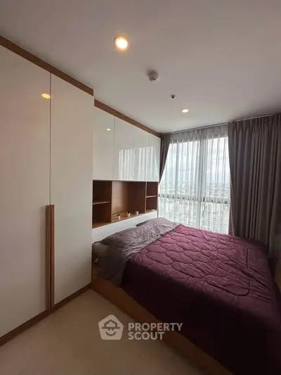 Modern bedroom with large window and built-in wardrobe in a high-rise apartment.