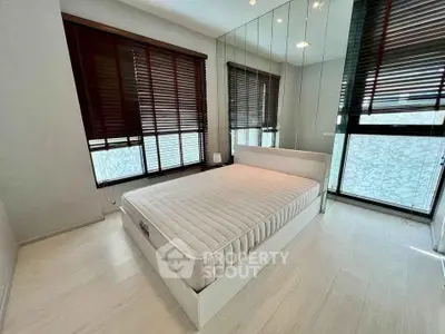 Modern minimalist bedroom with large windows and mirrored wall, featuring a sleek bed frame and natural light.