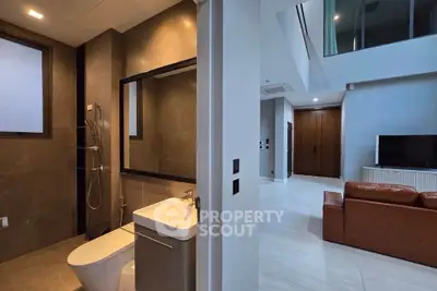 Modern interior with sleek bathroom and spacious living area featuring a leather sofa and flat-screen TV.