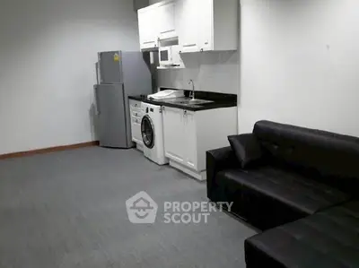 Modern studio apartment with compact kitchen and cozy living area, featuring a washing machine and sleek black sofa.