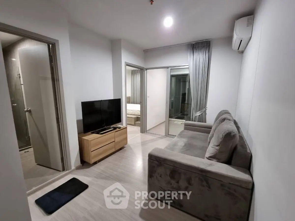 Modern living room with cozy sofa and TV, adjacent to bedroom and bathroom, featuring sleek design and neutral tones.