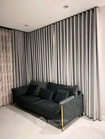 Elegant living room with plush black sofa and luxurious floor-to-ceiling curtains.