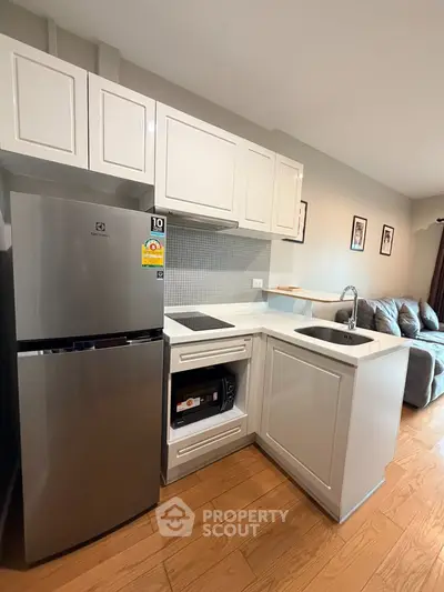 Modern compact kitchen with sleek appliances and cozy living area in open layout apartment.