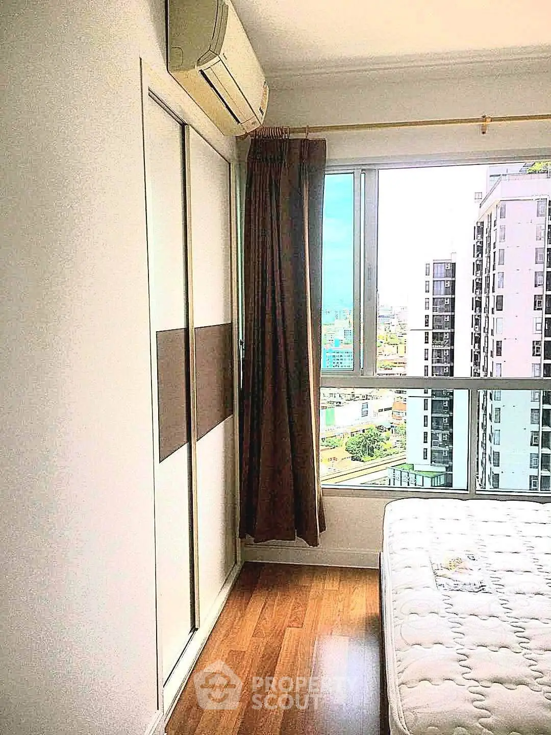 Bright bedroom with city view, featuring wooden flooring and air conditioning, perfect for urban living.