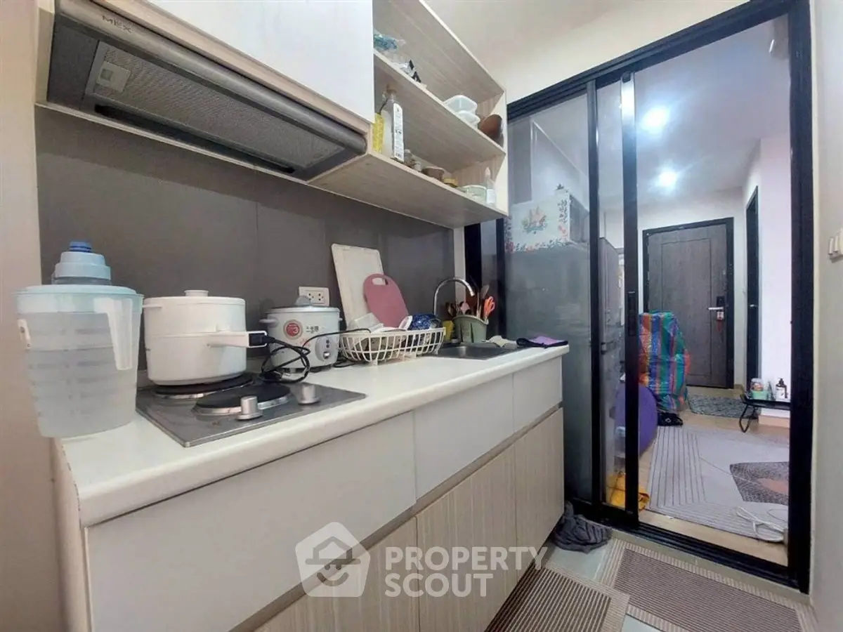 Compact kitchen with modern appliances and sliding glass door in cozy apartment.