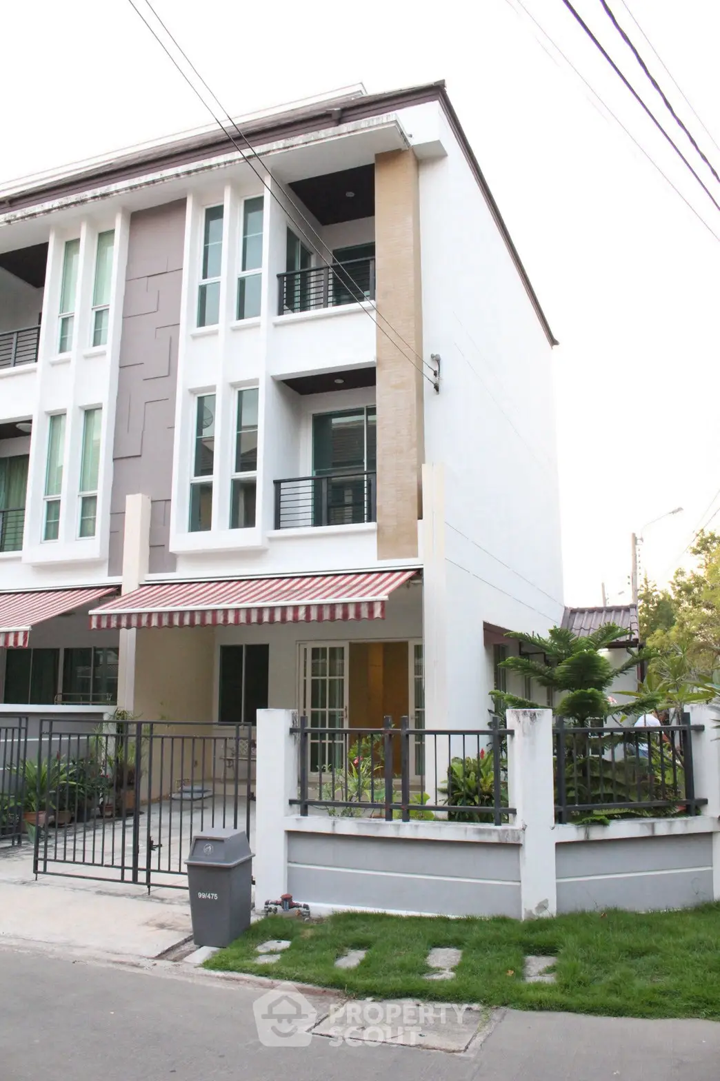 Modern three-story townhouse with stylish facade and small garden in urban setting.