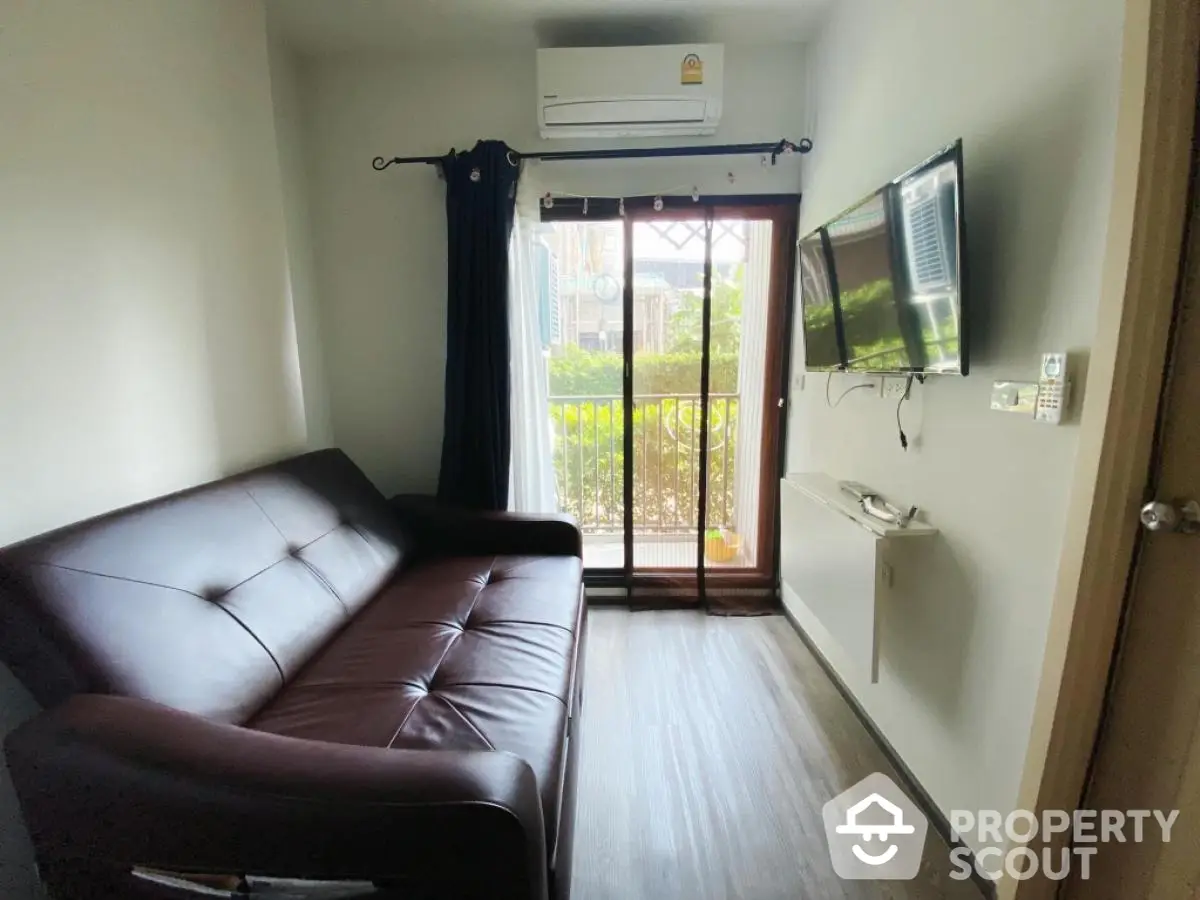 Cozy living room with modern sofa and wall-mounted TV, featuring a small balcony with garden view.