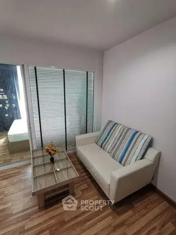Cozy living room with modern sofa and glass coffee table, featuring wooden flooring and sliding glass doors.
