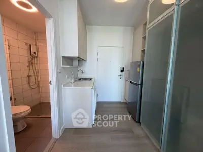 Compact modern apartment with sleek kitchen and bathroom, featuring a stylish glass partition and wood flooring.