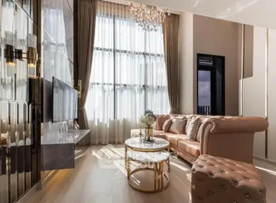 Luxurious living room with high ceilings, elegant chandelier, and plush leather sofa in a sunlit space.