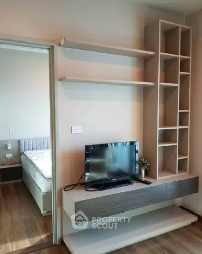 Modern living room with sleek TV unit and open shelving, adjacent to a cozy bedroom.