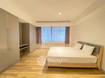 Spacious modern bedroom with wooden flooring and large window for natural light.