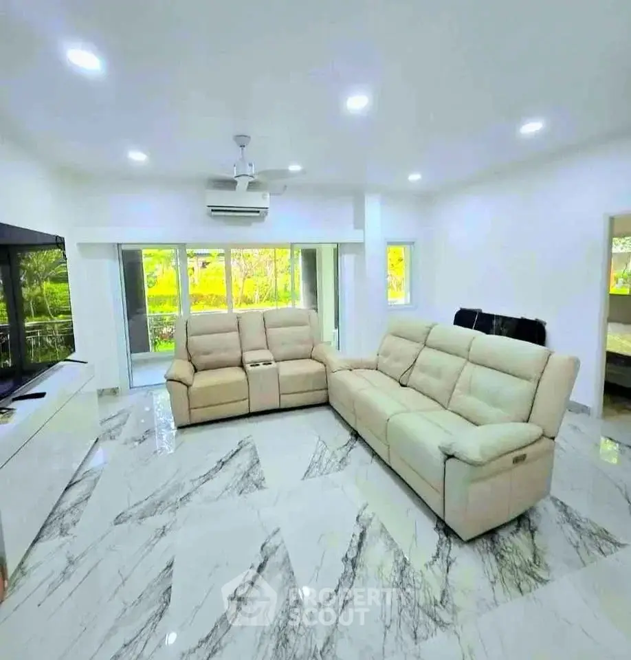 Spacious modern living room with elegant marble flooring and plush sofas, offering a serene garden view.