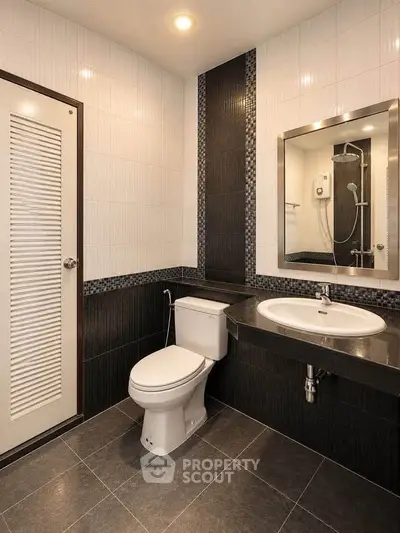 Modern bathroom with sleek black and white tiles, featuring a toilet and stylish sink.