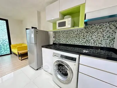 Modern kitchen with washing machine, fridge, and microwave in stylish apartment.