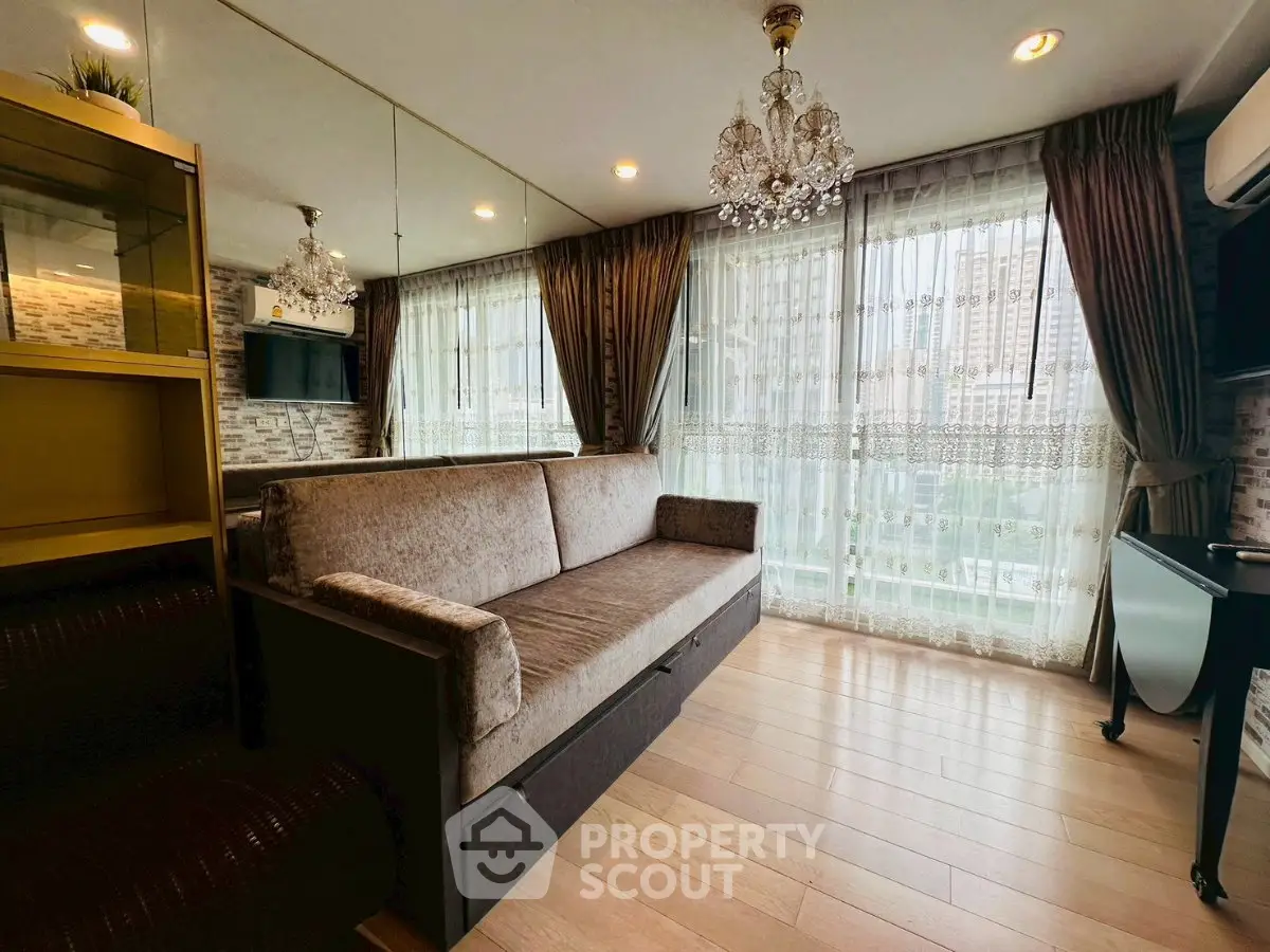 Luxurious living room with elegant chandelier and city view, featuring plush sofa and floor-to-ceiling windows.