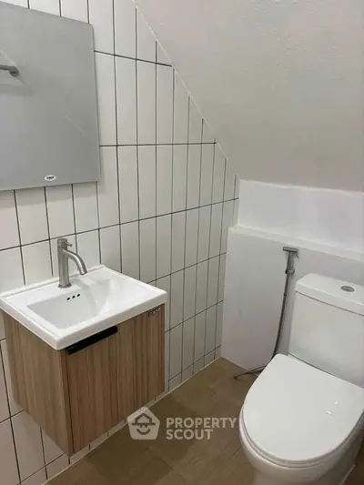 Modern bathroom with sleek fixtures and minimalist design under sloped ceiling.
