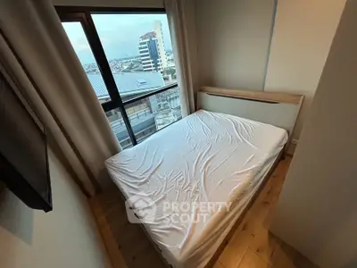 Cozy bedroom with a view, featuring a neatly made bed and large window overlooking the cityscape.