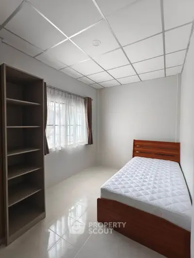 Minimalist bedroom with single bed and shelving unit, bright natural light.