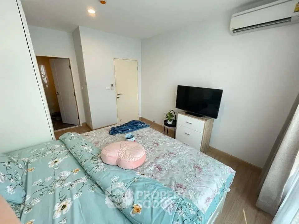 Cozy bedroom with floral bedding, wall-mounted TV, and air conditioning in modern apartment.