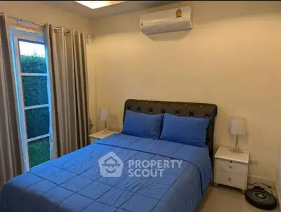 Cozy bedroom with blue bedding and modern decor, featuring a window view of lush greenery.