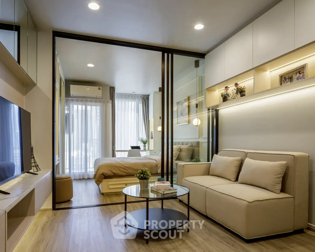 Modern living room with glass partition leading to cozy bedroom, featuring elegant decor and natural light.