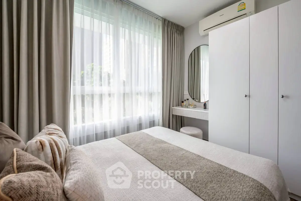 Cozy bedroom with modern decor, large window, and stylish vanity area.