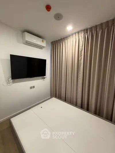 Modern bedroom with wall-mounted TV and air conditioning, featuring elegant curtains and minimalist design.