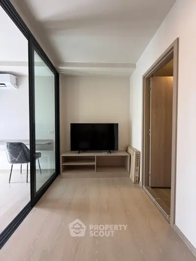 Modern living room with TV, glass partition, and stylish chair in a bright apartment.