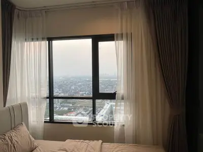Cozy bedroom with stunning city view through large window, featuring elegant curtains and modern decor.