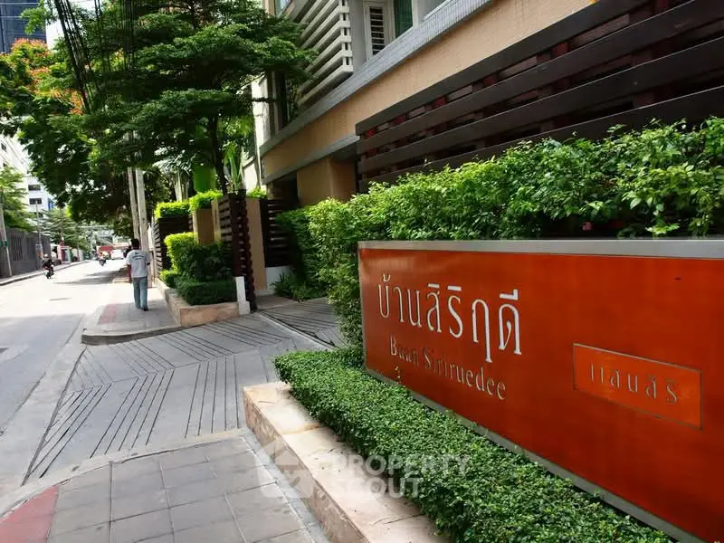 Elegant building entrance with lush greenery and modern signage in urban setting.