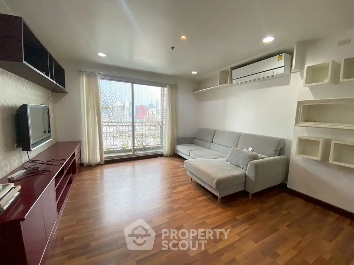 Spacious living room with modern decor and city view, featuring a comfortable sofa and wall-mounted TV.