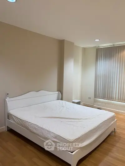 Spacious bedroom with elegant white bed and natural light through large window blinds.