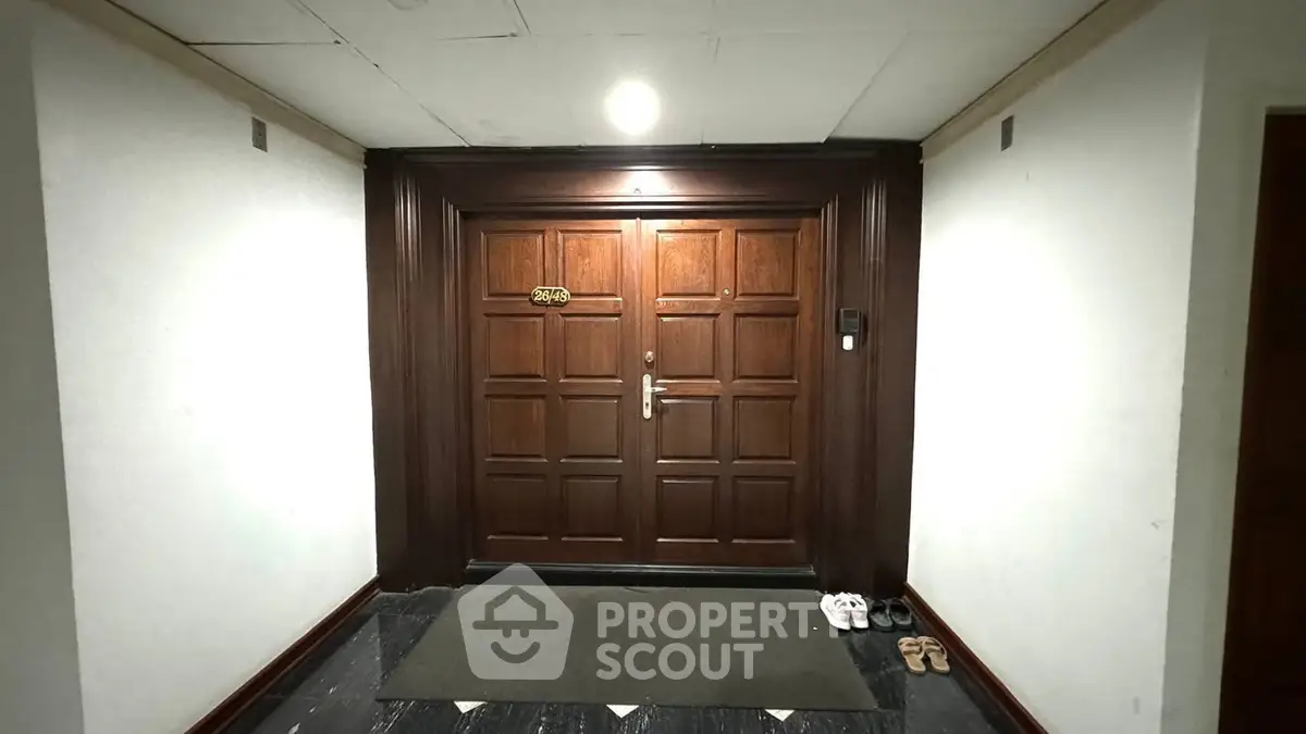 Elegant apartment entrance with wooden double doors and sleek hallway lighting.