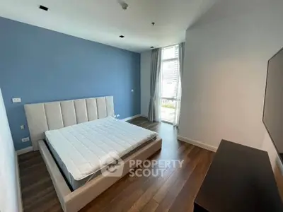 Spacious modern bedroom with large window and hardwood floors in luxury apartment.
