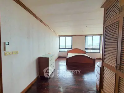 Spacious bedroom with wooden flooring and large windows offering natural light.