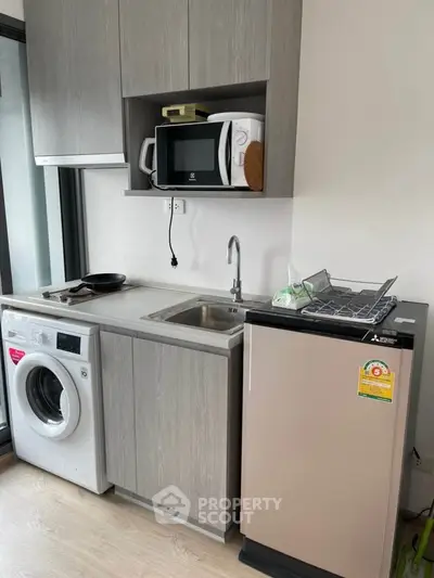 Modern compact kitchen with washing machine and microwave in sleek apartment.