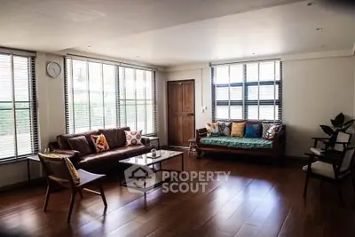 Spacious living room with wooden flooring and large windows, featuring stylish furniture and natural light.