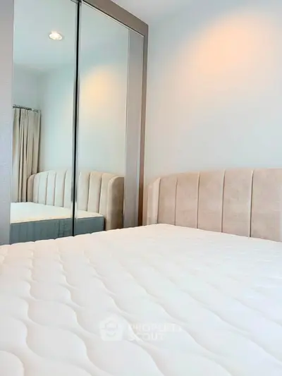 Modern bedroom with mirrored wardrobe and plush headboard in a cozy apartment.