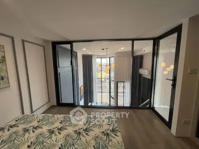 Modern bedroom with large windows and balcony view, featuring stylish decor and ample natural light.