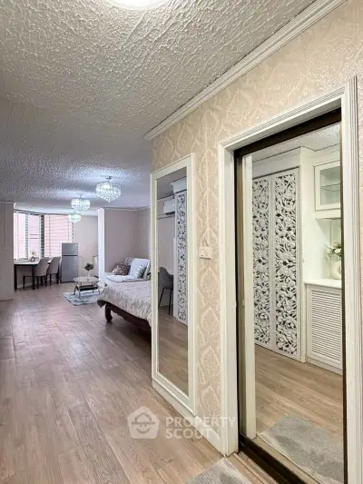 Spacious bedroom with elegant decor and large mirror, featuring wooden flooring and stylish lighting.