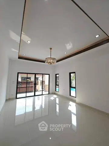 Spacious living room with elegant chandelier and large windows opening to a pool view.
