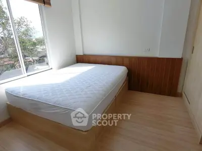 Bright bedroom with large window and wooden flooring, featuring a comfortable bed and serene view.