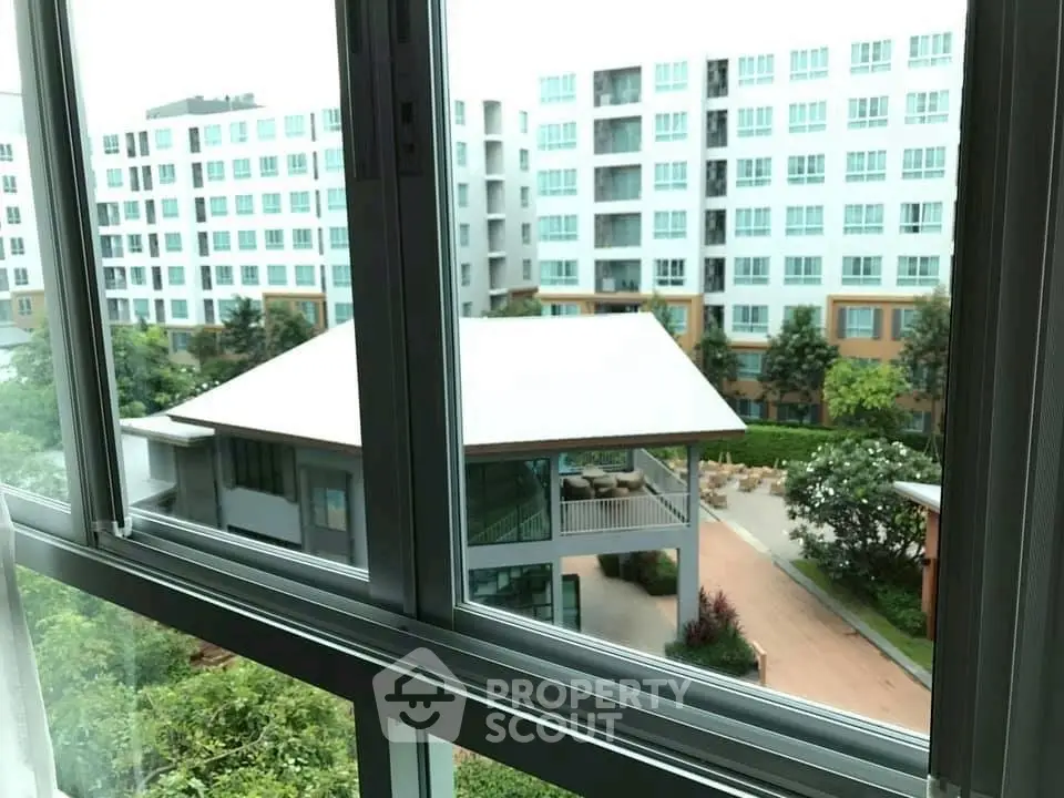 Modern apartment complex view from window with lush greenery and communal area.