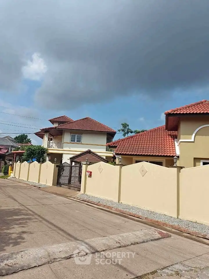 Charming suburban house with red roof and fenced yard under a cloudy sky