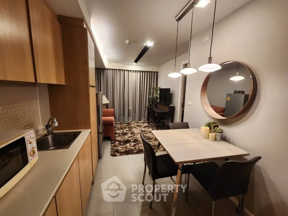 Modern kitchen with open layout flows seamlessly into cozy living area, featuring stylish pendant lighting and a chic round mirror, perfect for entertaining.