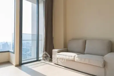 Modern living room with large windows and city view, featuring a comfortable beige sofa.