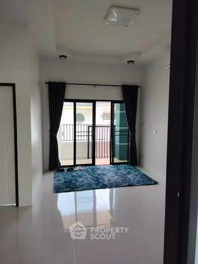 Spacious living room with large windows and balcony access, featuring modern curtains and a plush rug.