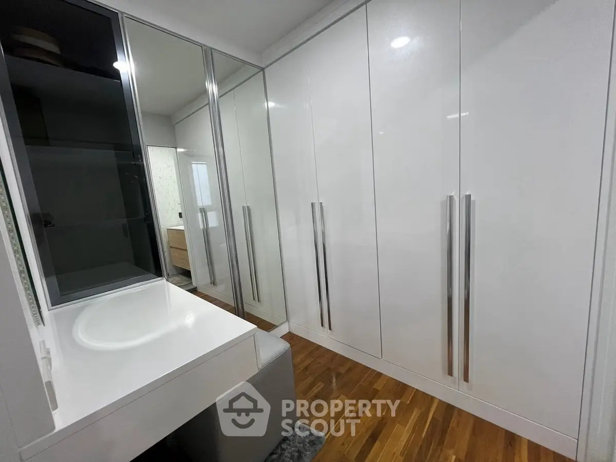 Spacious modern walk-in closet with sleek white cabinetry and wooden flooring.